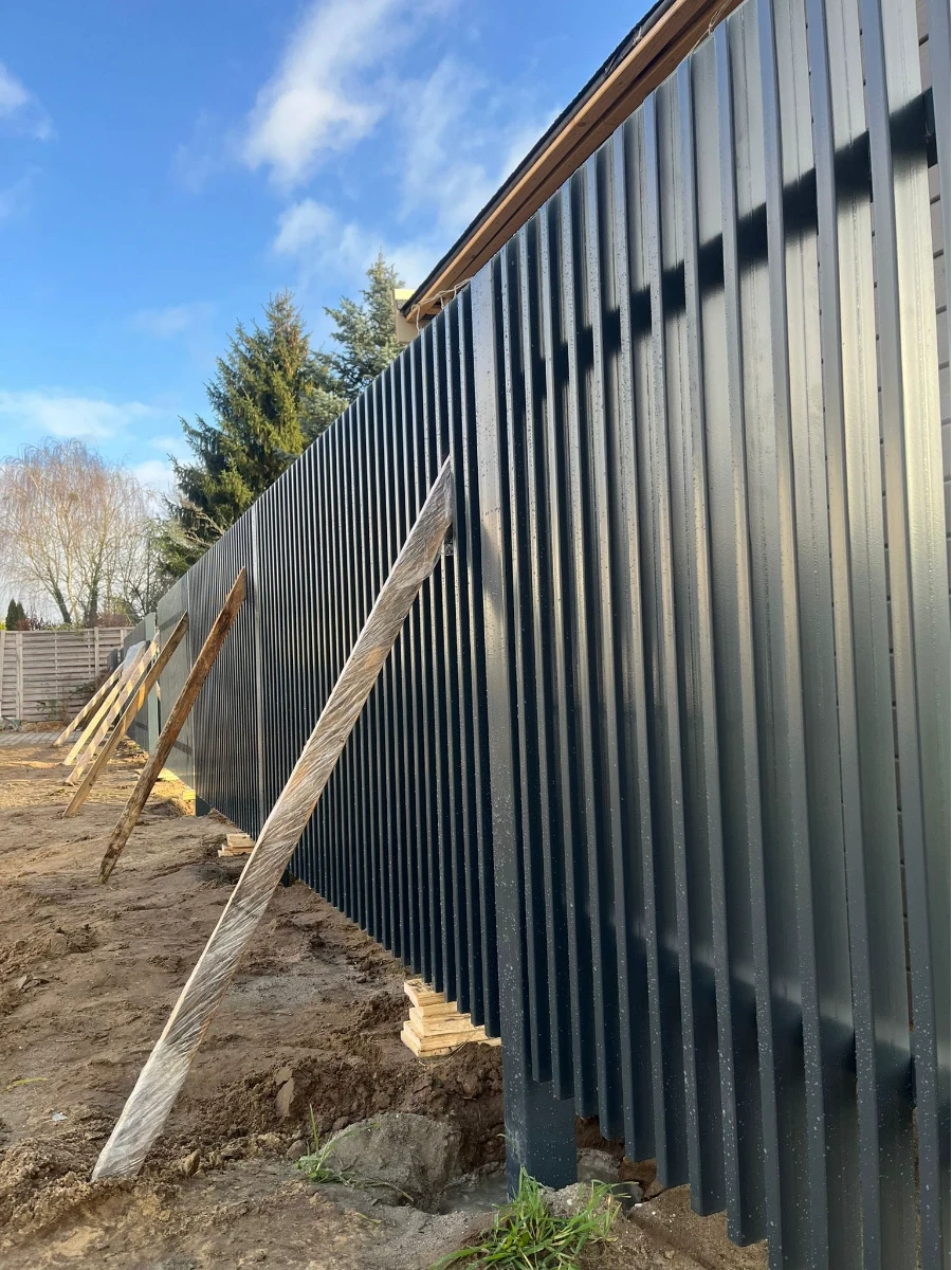 Schwarzer Metall-Lamellenzaun mit Holzstützen während Montage