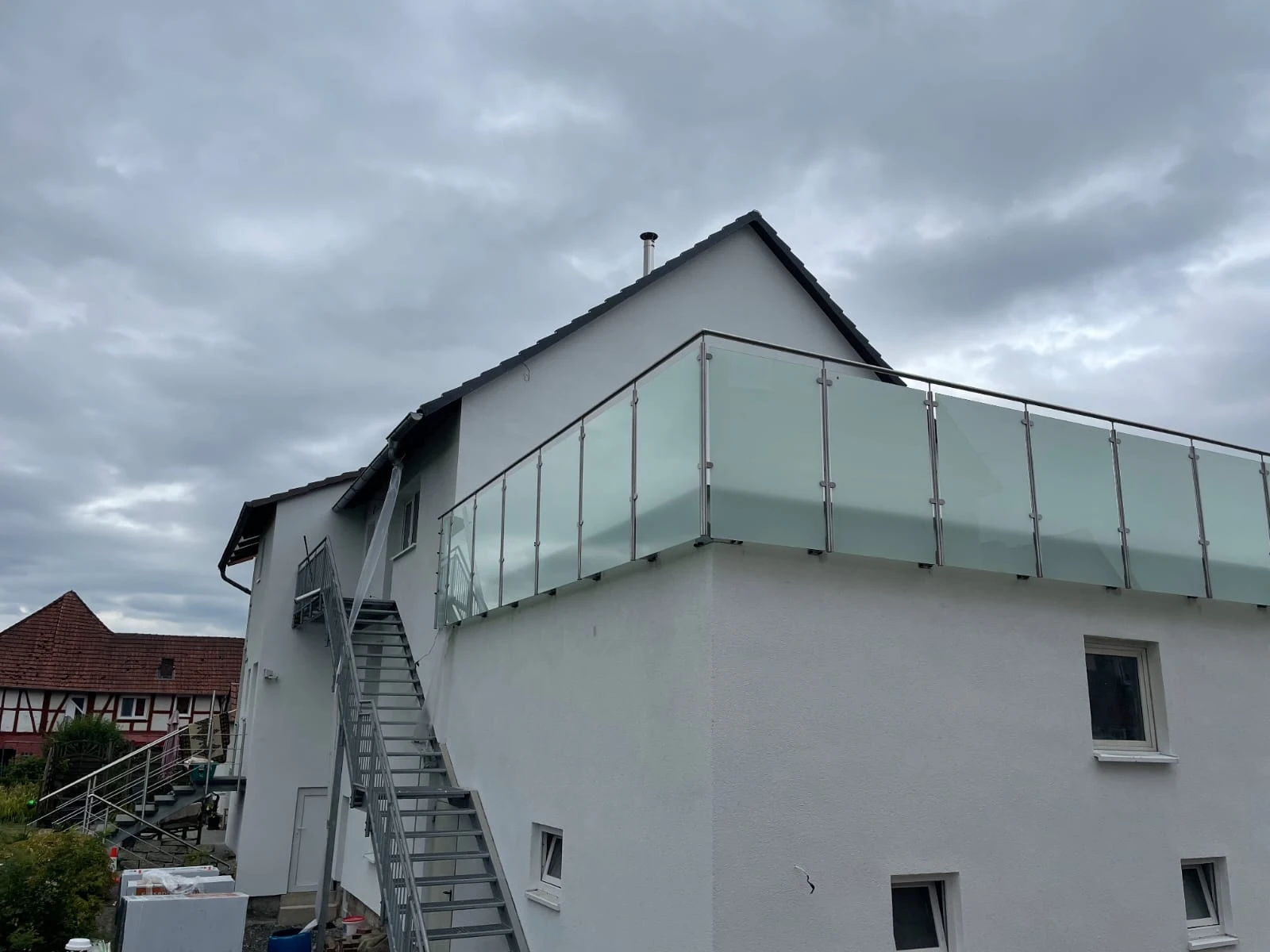 Moderne Glas-Geländer mit Edelstahlpfosten an weißer Hausfassade und Außentreppe