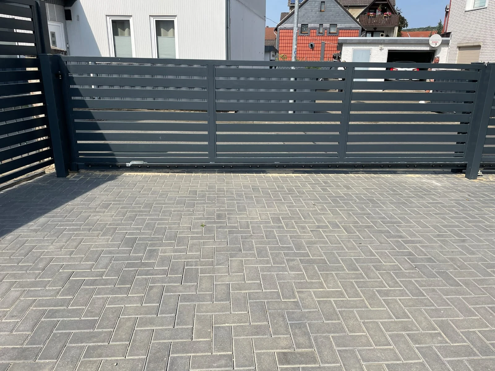 Graues Aluminium-Eingangstor mit horizontalen Lamellen vor gepflasterter Einfahrt
