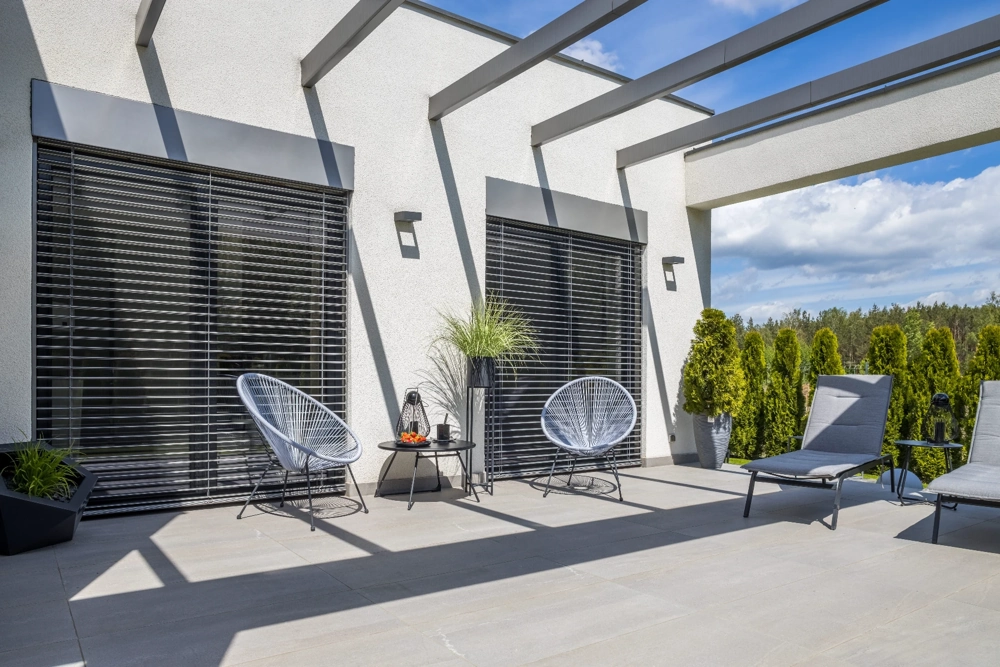Terrasse mit Pergola, bequemen Sesseln, Sonnenliegen und Fenstern mit Außenjalousien
