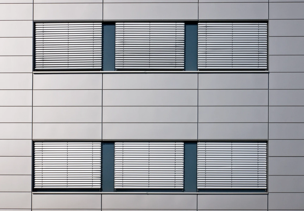 Fassadenansicht eines modernen Gebäudes mit geschlossenen Außenjalousien vor rechteckigen Fenstern
