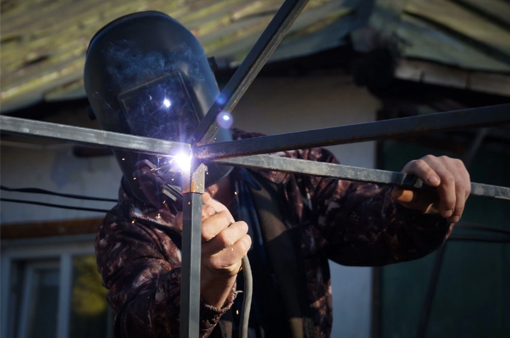 Schweißer führt individuelle schweißarbeiten an Stahlrahmen mit Schutzhelm im Außenbereich aus