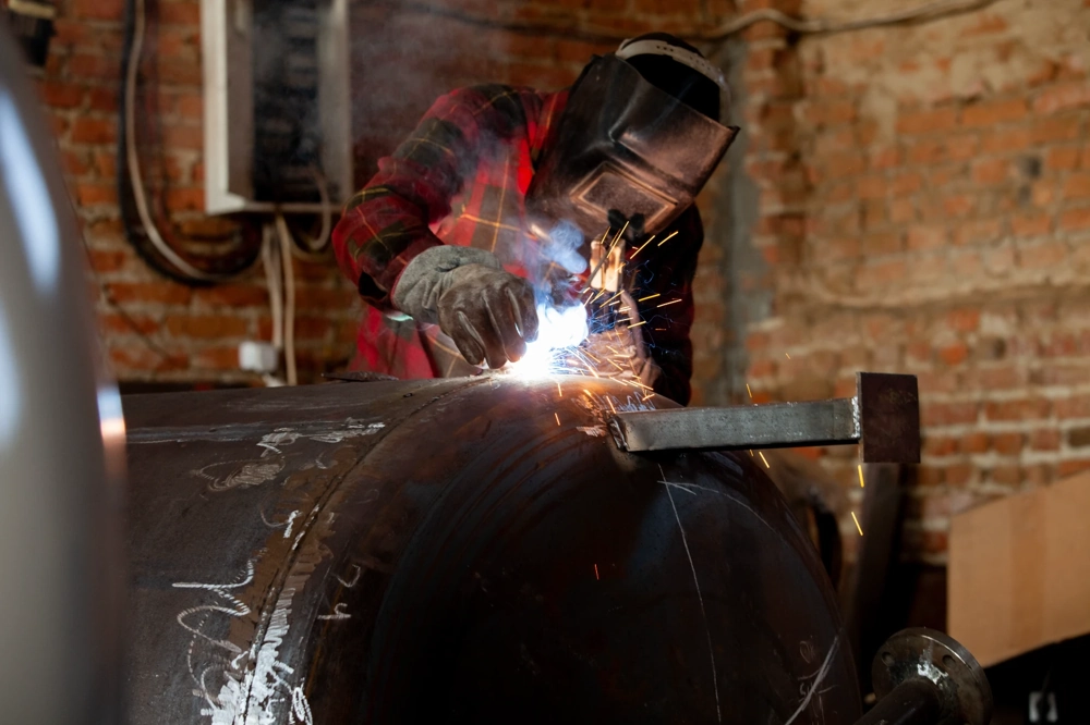 Individuelle schweißarbeiten an großem Metallzylinder in Werkstatt mit schutzhelm und funkenflug